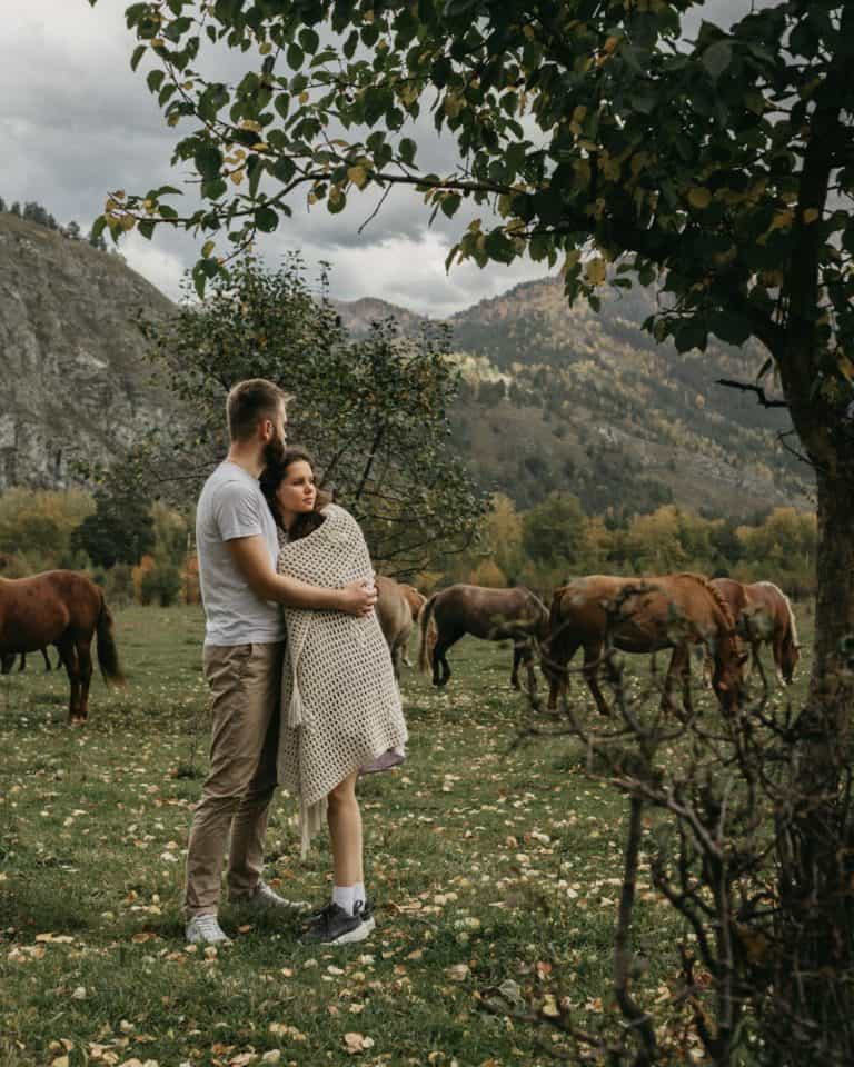 Couple hugging against mountains and horses